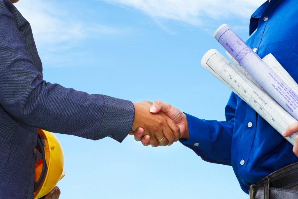 Two contractors shake hands with blue sky background