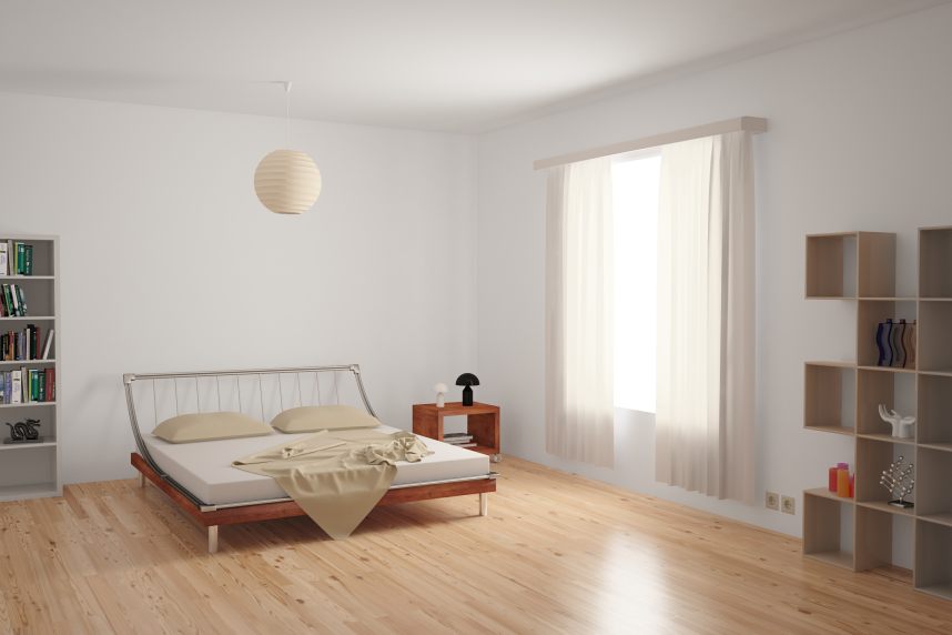 Modern bedroom interior with minimalistic furnishing in neutral colours on an uncarpeted hardwood floor.